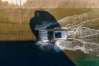 an overhead view of a white car driving down the road near the water's edge