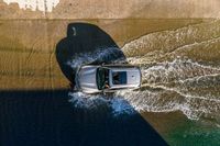 an overhead view of a white car driving down the road near the water's edge