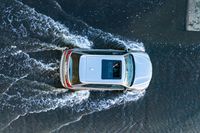 an aerial view of a white vehicle driving through water in the middle of a body of water