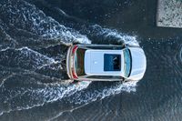 an aerial view of a white vehicle driving through water in the middle of a body of water