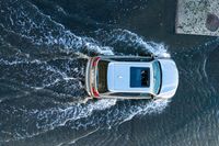 an aerial view of a white vehicle driving through water in the middle of a body of water