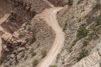 a jeep is traveling down a winding mountain side road, in front of a rocky cliff