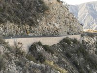 a road is winding away from the mountainside and steep slope of the valley, which runs into it