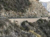 a road is winding away from the mountainside and steep slope of the valley, which runs into it