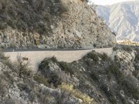 a road is winding away from the mountainside and steep slope of the valley, which runs into it