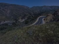 the view of a winding winding road and mountains is at dusk in the background, and there are no cars on the way