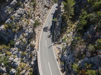 the road is winding between the cliffs and trees, with two motorcycles on it in mid distance