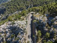 the road is winding between the cliffs and trees, with two motorcycles on it in mid distance