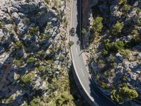 the road is winding between the cliffs and trees, with two motorcycles on it in mid distance