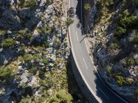 the road is winding between the cliffs and trees, with two motorcycles on it in mid distance