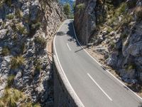 the road is winding between the cliffs and trees, with two motorcycles on it in mid distance