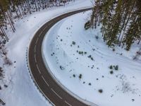 an aerial shot of a winding road through a forest covered in snow, in the late winter