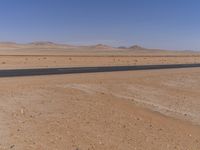 empty road near desert area with mountains in background, no people yet on it, in the distance are bushes and sparse clouds