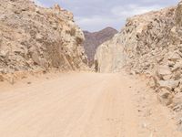 a small vehicle traveling across a barren road between some large rocks and boulders on one side