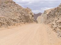 a small vehicle traveling across a barren road between some large rocks and boulders on one side