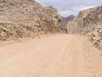 a small vehicle traveling across a barren road between some large rocks and boulders on one side