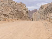 a small vehicle traveling across a barren road between some large rocks and boulders on one side