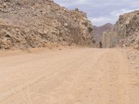 a small vehicle traveling across a barren road between some large rocks and boulders on one side