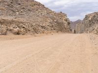 a small vehicle traveling across a barren road between some large rocks and boulders on one side