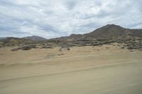 a view out of a car window showing desert areas with sand and mountains in the distance