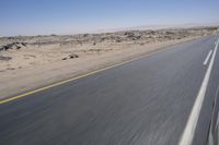 the view from a speeding motorcycle on an empty desert highway with a person riding an automobile