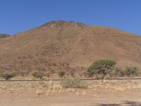 a man in white shirt standing near a desert hill by himself on the side of a road