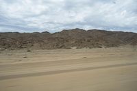 a dirt mountain near a large open field of dry grass and rocks in a desert