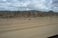 a dirt mountain near a large open field of dry grass and rocks in a desert