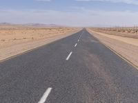 empty road near desert area with mountains in background, no people yet on it, in the distance are bushes and sparse clouds