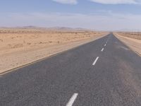 empty road near desert area with mountains in background, no people yet on it, in the distance are bushes and sparse clouds