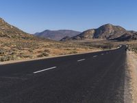 a deserted road in the desert during the day time with mountains in the background and the road is empty