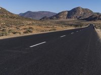 a deserted road in the desert during the day time with mountains in the background and the road is empty