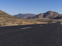 a deserted road in the desert during the day time with mountains in the background and the road is empty