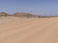 a man riding a bike down a dirt road next to a dirt mountain range next to power lines