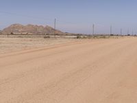 a man riding a bike down a dirt road next to a dirt mountain range next to power lines