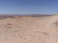 the dog is walking through the rocky desert field with its head in the air near a road