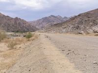 a man is riding a motorcycle down the desert road near mountains and a sign on a rock