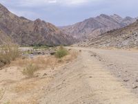 a man is riding a motorcycle down the desert road near mountains and a sign on a rock