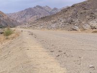 a man is riding a motorcycle down the desert road near mountains and a sign on a rock