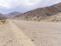 a man is riding a motorcycle down the desert road near mountains and a sign on a rock