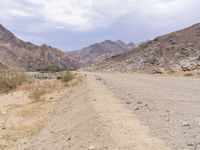 a man is riding a motorcycle down the desert road near mountains and a sign on a rock