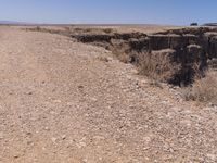 a man sitting next to a cliff looking at the side of a road in a dry grass field