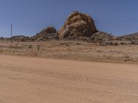 a big rock in the middle of an open desert with dirt on ground and blue sky above