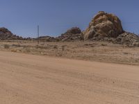 a big rock in the middle of an open desert with dirt on ground and blue sky above