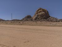 a big rock in the middle of an open desert with dirt on ground and blue sky above