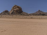 a big rock in the middle of an open desert with dirt on ground and blue sky above