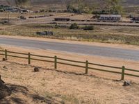 a small road that has a fence near it in the middle of nowhere with the dirt surrounding it and a lone horse sitting on top