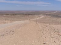 a dirt road winding into the desert with a sign on top of it and telephone poles in the distance