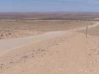 a dirt road winding into the desert with a sign on top of it and telephone poles in the distance