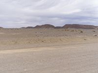 an empty desert with dirt and sand hills behind it and clouds overhead over the mountains